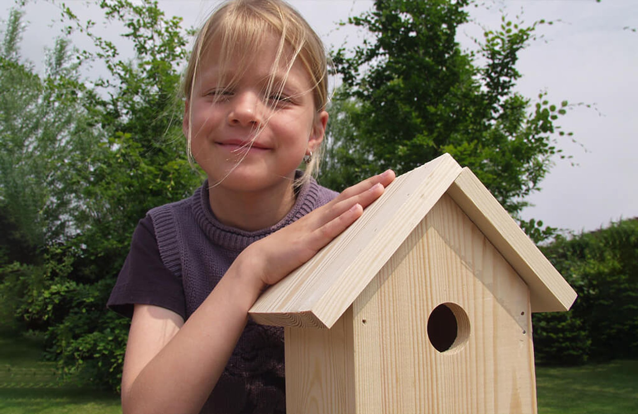 Kind lächelt während es das zusammengebaute Vogelhaus vorstellt